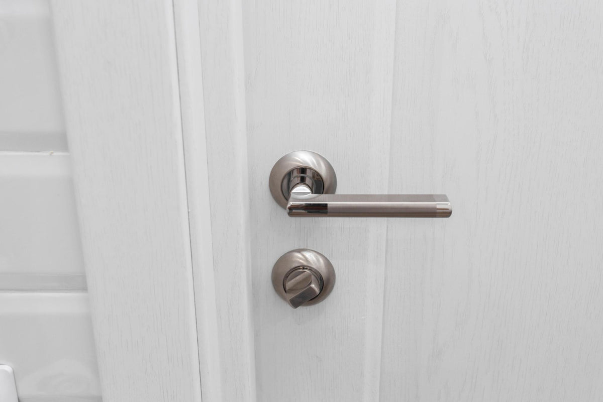 A modern satin nickel door handle and matching deadbolt set mounted on a white paneled door.